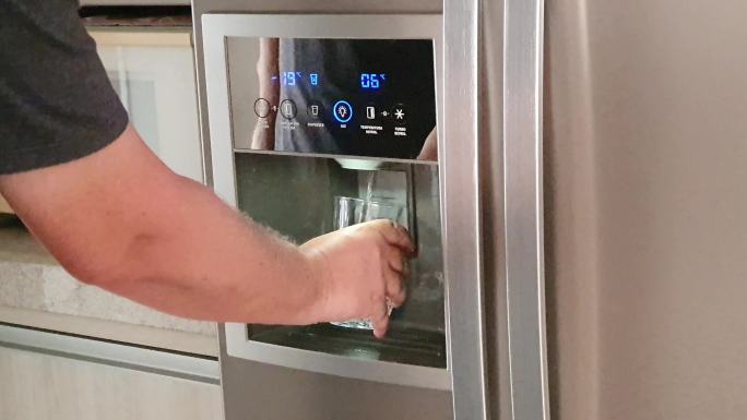 男子在冰箱饮水机前抓起一杯水。