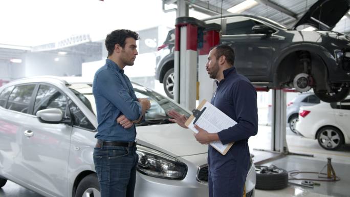 在一家汽车修理店，机修工主管将汽车交给男性客户，双方看起来都很高兴地握手