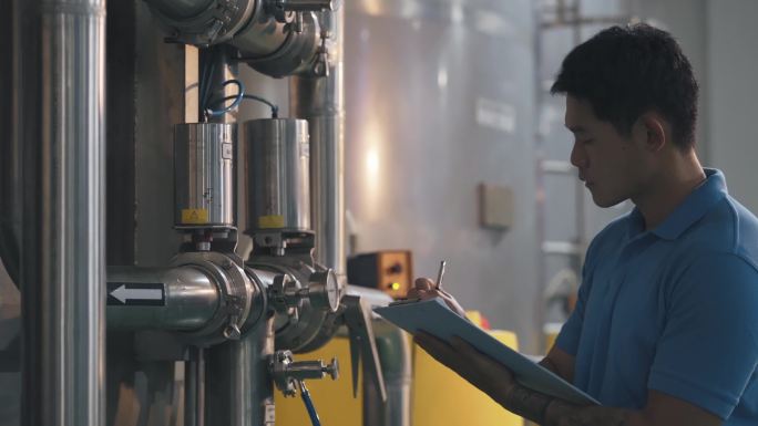 亚裔中国技师维护工程师记录水箱中的仪表读数瓶装水厂的日常质量控制书写在剪贴板上