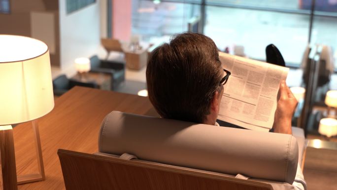 商务人士在机场贵宾休息室放松阅读新闻报纸的后视图