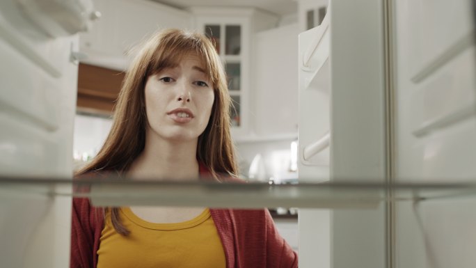 感到饿的女子打开冰箱是空的感到饥饿沮丧破