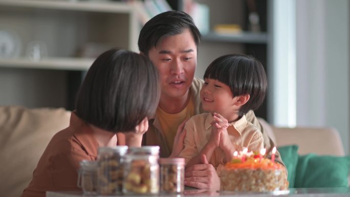 亚裔中国家庭闭上眼睛在生日蛋糕前许生日愿望，然后在客厅吹生日蜡烛庆祝儿子生日