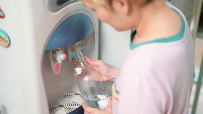 女人在家里用玻璃瓶装水净水器