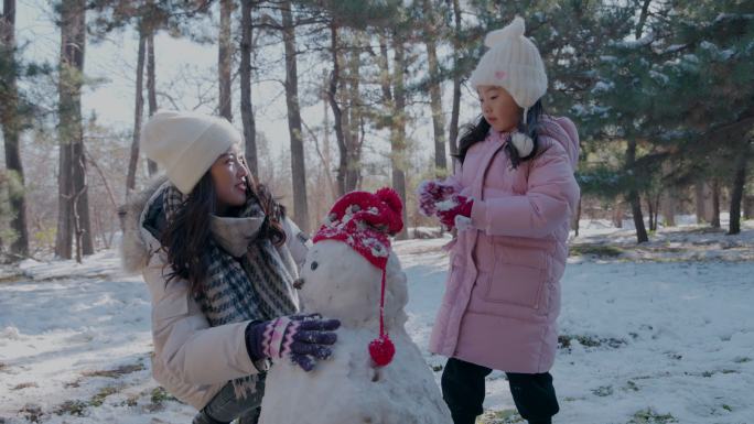 年轻妈妈和女儿在雪地里堆雪人