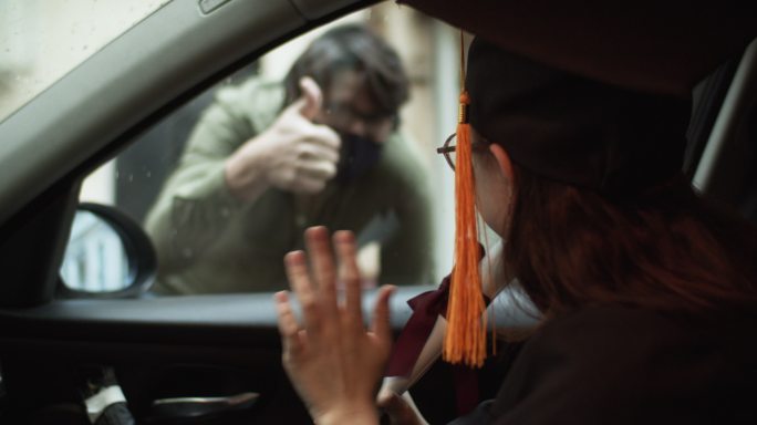 一个十几岁的女孩穿着毕业礼服，戴着毕业帽，车上有文凭，一个男人在街上向她打招呼