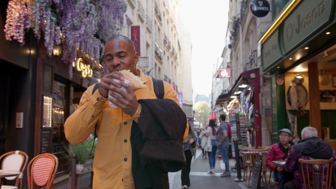 男性游客在巴黎漫步，吃着煎饼