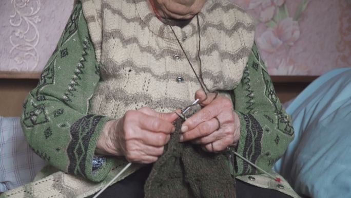 一位老年人编织精细美观，一位奶奶双手布满皱纹的特写镜头，正在制作一件新的冬季毛衣，积极的退休人员。