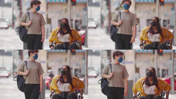 在城市街，一位戴着面具的亚洲中国中年女性与残疾印度女性朋友在轮椅上并肩行走