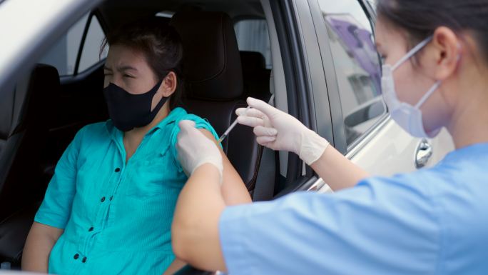驱车前往疫苗接种站，年轻的亚洲医生为那些驾驶私人汽车前往接种站的人注射新冠病毒-19疫苗。