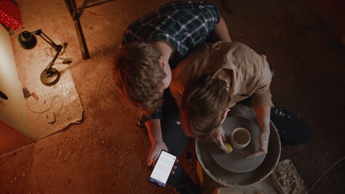 斯洛·莫（SLO-MO）年轻夫妇在陶艺工作室用智能手机制作粘土