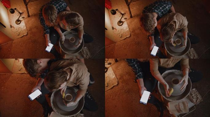 斯洛·莫（SLO-MO）年轻夫妇在陶艺工作室用智能手机制作粘土