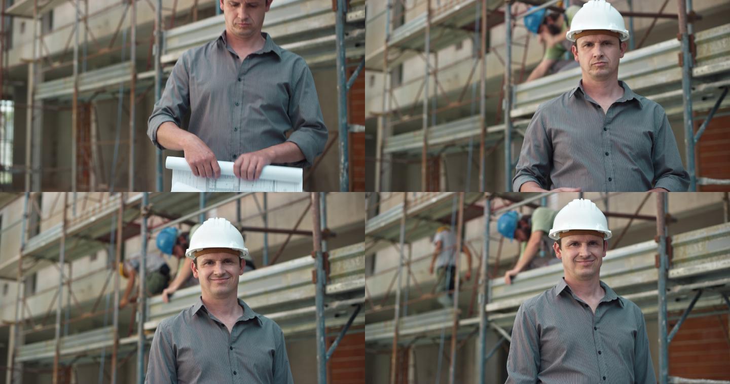 男建筑师戴着白色头盔，在施工现场滚动平面图，对着摄像机微笑