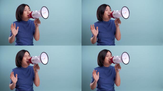 快乐的亚洲女人用扩音器在蓝色背景上做出孤立的叫喊手势。4K视频