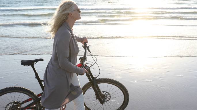 一名女子在空旷的海滩上推着自行车