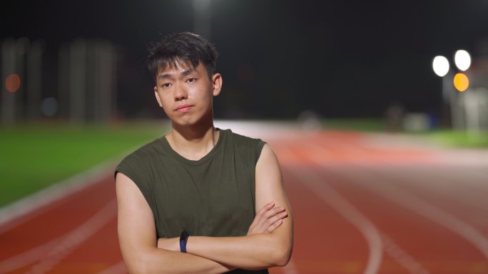 雨后的夜晚，筋疲力尽的男运动员站在全天候田径场上看着摄像机