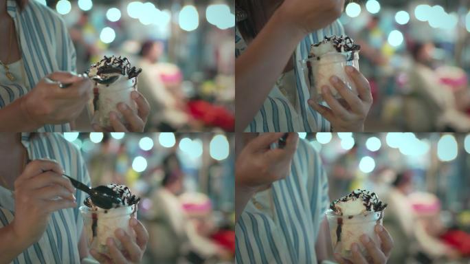 一位亚洲妇女在夜市的杯子里吃着美味的冰淇淋甜点。泰国著名的美食街甜品。泰国街头美食。