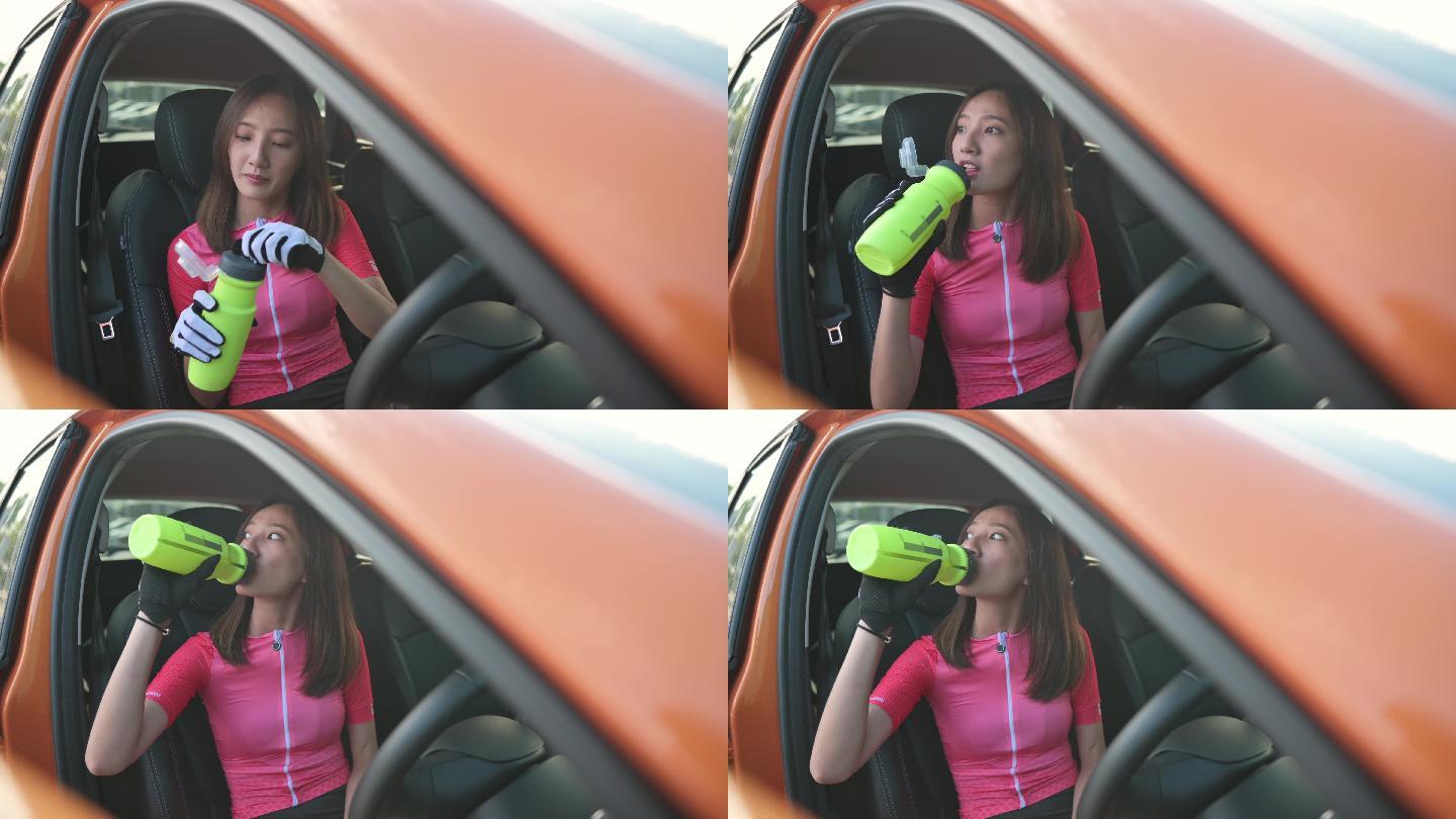 周末早上，中国亚裔年轻女子坐在驾驶座上喝水，准备进行公路旅行