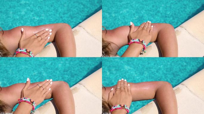 在一个炎热、阳光明媚的日子里，一个女人在游泳池边把防晒霜涂在胳膊上。