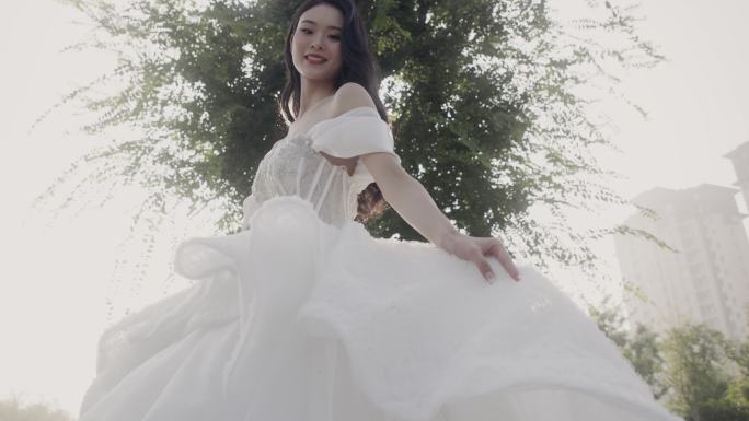 穿着白色长尾婚纱的年轻亚洲女孩对着镜头微笑，新娘快乐