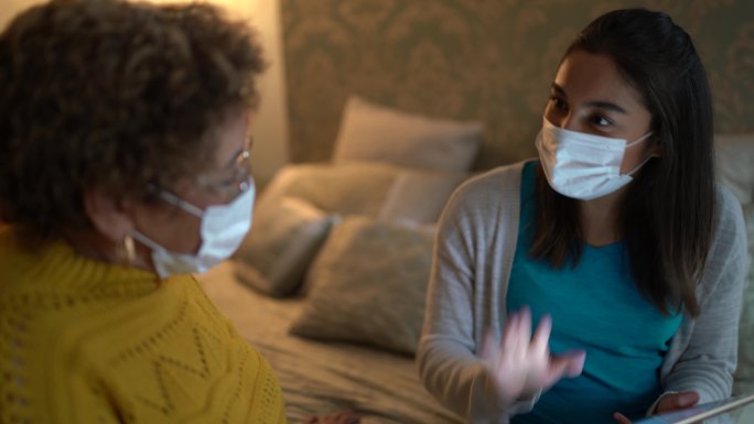 家访期间，医生在卧室与老年患者交谈-戴上防护面罩