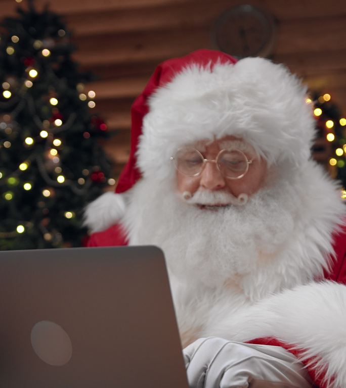 穿着漂亮服装的圣诞老人正在和一个他在笔记本电脑视频通话中听不到的人发短信