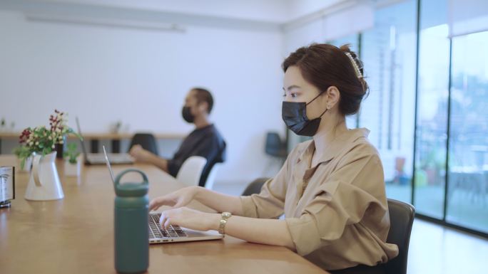 戴着口罩在笔记本电脑上工作的亚洲女商人