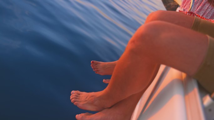 日落时分，坐在游艇舷侧甲板上的一名男子的懒散双腿