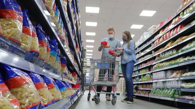 一对戴口罩的年轻夫妇在超市过道上按营养标签选择食物
