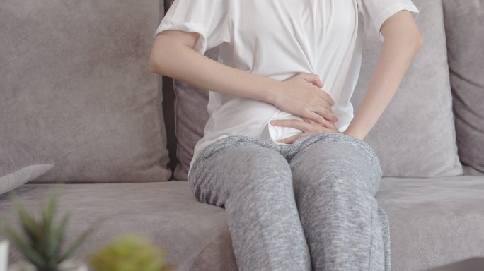 一名亚洲女性坐在家中沙发上时腹痛