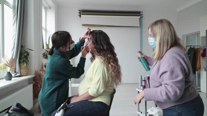 化妆师和美发师在工作室拍摄前与时装模特合作。