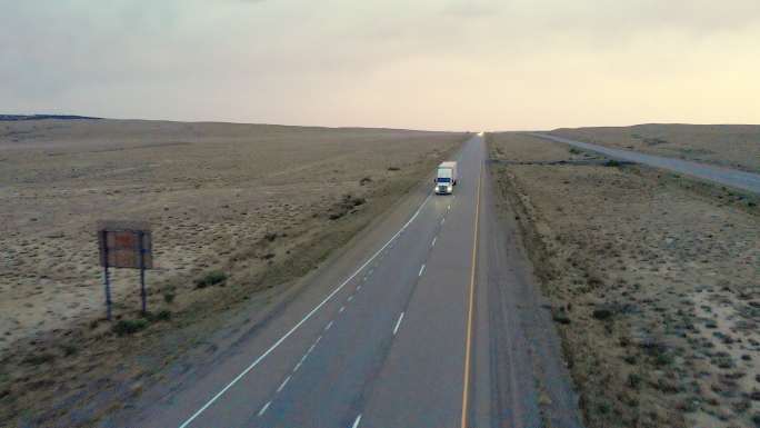 犹他州沙漠黄昏时分，无人驾驶飞机拍摄了一辆半卡车，车上的灯亮着
