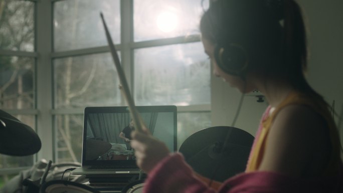 在起居室练习电子鼓的年轻女子。在笔记本电脑上观看播放教程