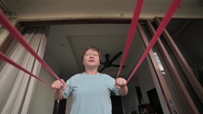 亚洲中国中年女性在阳台上进行阻力带家庭训练