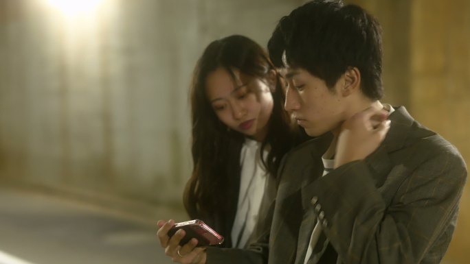 日本z一代夫妇一边聊天一边看着黑暗通道上的智能手机