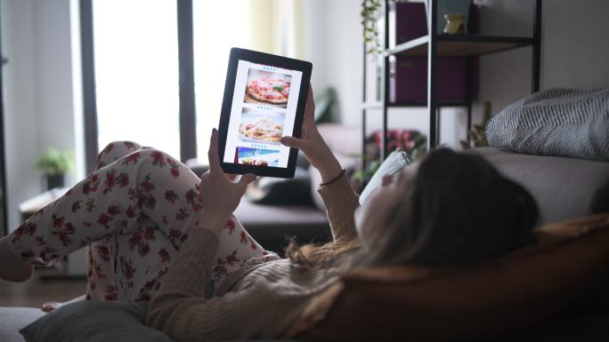 女性在家放松，通过数字平板电脑在线订购食物。