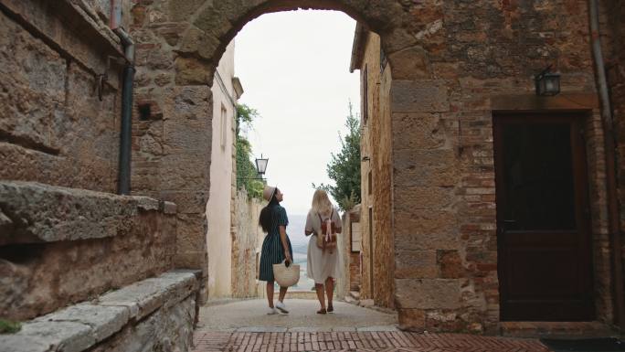 SLO MO两名女性游客穿过Pienza镇的一条狭窄小巷