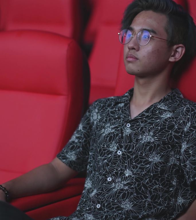 中国亚裔少年独自在电影院看电影，表情茫然