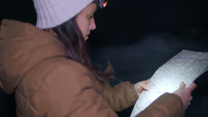 冬季旅行者在夜间看地图，一位年轻女性游客在冬季山脉中行走的中景照片，肖像，旅游，探险，旅游，决心，运