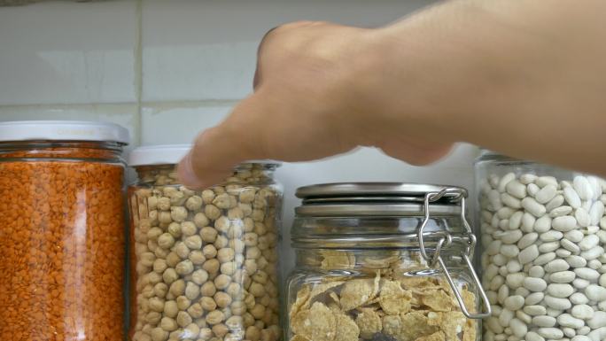 厨房食品储藏室货架上装满豆类的罐子是由一名男子整理的。