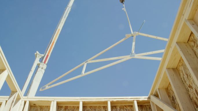 晴朗的日子里，一台液压起重机将一个带框架的木屋架放在施工现场的一栋带框架的房子上