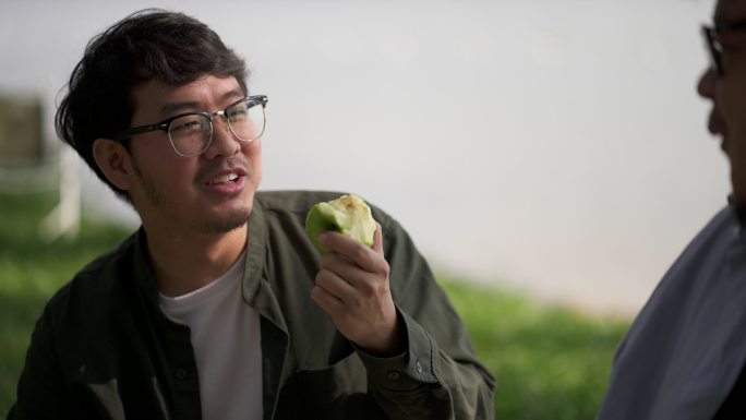 特写镜头：吃绿苹果的人和他在河边的朋友聊天。
