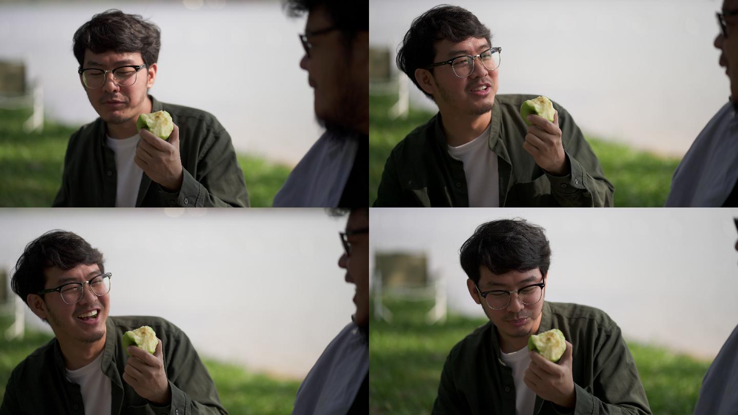 特写镜头：吃绿苹果的人和他在河边的朋友聊天。