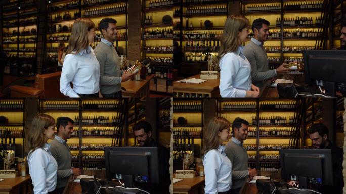 一对拉丁美洲夫妇在一家品酒酒窖里走上前去结账，并将酒瓶递给男收银员
