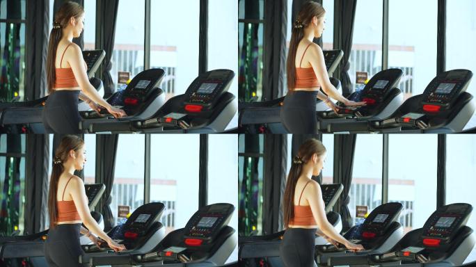 亚洲美丽的年轻运动女性，在跑步机上跑步，喝矿泉水，在健身房的智能手表上查看运动数据。