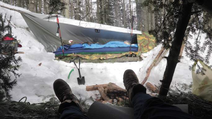 一名男子在冬季林地露营地放松的个人视角