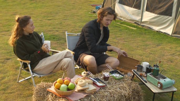 美丽的白人白人年轻夫妇在日出时分野餐。男人和女人喝咖啡和热茶，背景是草原和山脉。