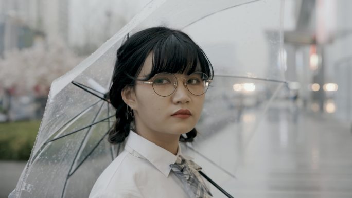 可爱的亚洲女学生，穿着校服，打着雨伞，站在街上