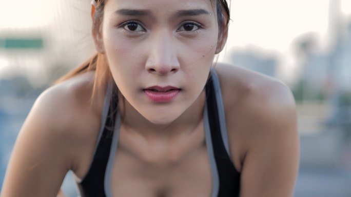 筋疲力尽的肌肉发达的亚洲女性抬起头看着镜头。她满身大汗，努力喘口气，保持社交距离以防止冠状病毒或新冠