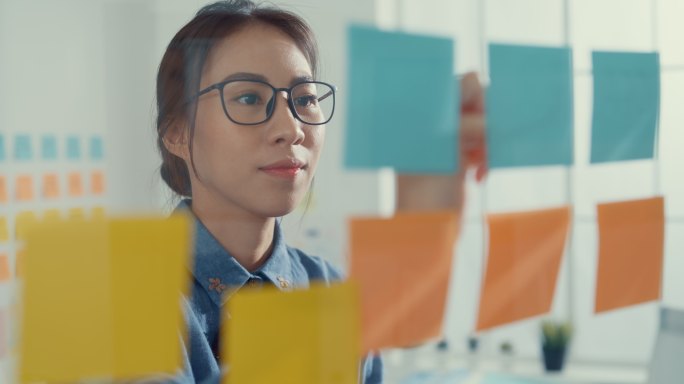 年轻的女商人在彩色的便笺上写字，在创意办公室开发商业项目。