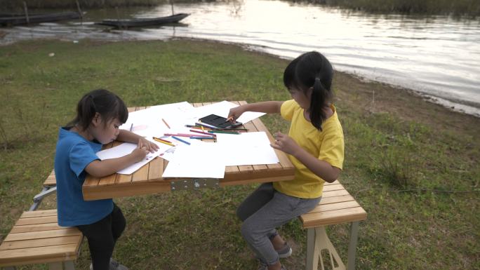 兄弟姐妹用彩色铅笔在纸上画卡通的场景，教育背景库存